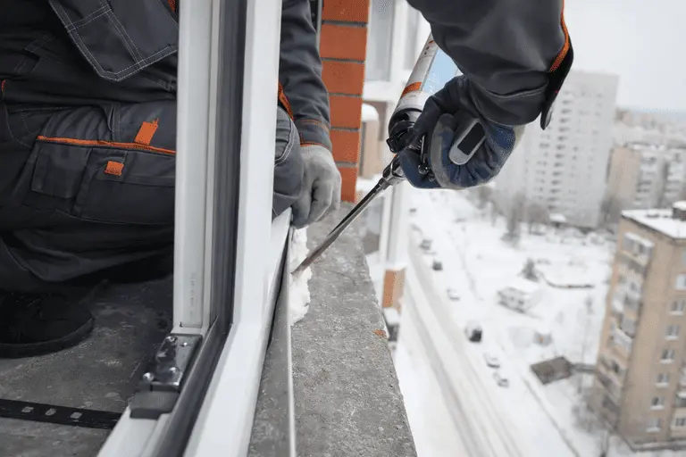 Монтажник заполняет монтажный шов окна монтажной пеной с наружной стороны здания